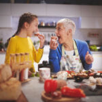 Senior woman with her grandchild in the kitchen having fun while preparing and tasting food.
