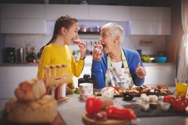 Senior woman with her grandchild in the kitchen having fun while preparing and tasting food.